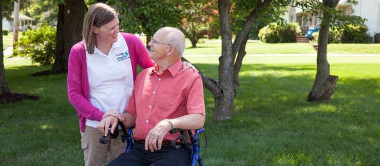 Female care worker provides companionship to elderly man in wheelchair during a trip outdoors.