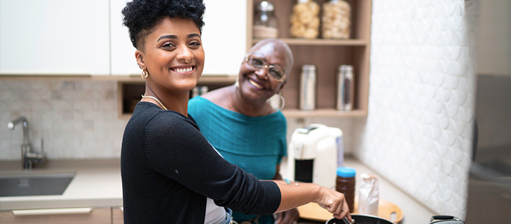 Adult daughter helps senior mother with cooking responsibilities in the kitchen.